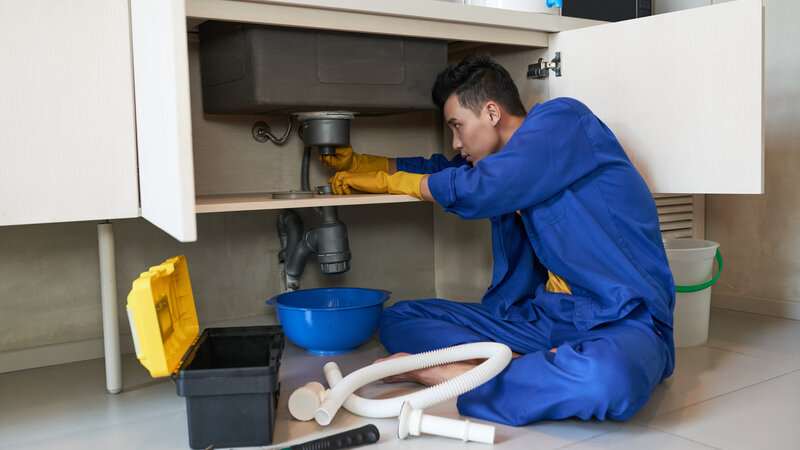 Professional plumber using drain snake to clear clogged drain - Warren Brothers Plumbing serves Bastrop, Austin, and Elgin TX