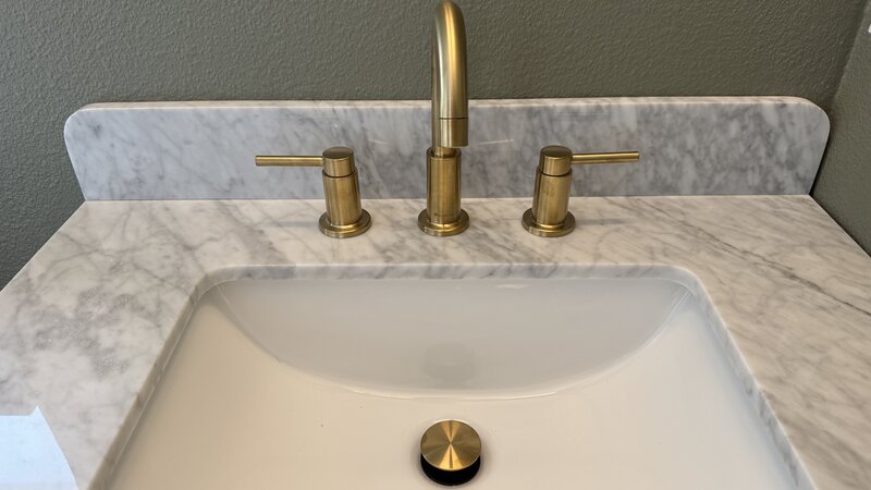 Modern brushed gold faucet installed on marble bathroom vanity - Warren Brothers Plumbing serves Bastrop, Austin, and Elgin TX