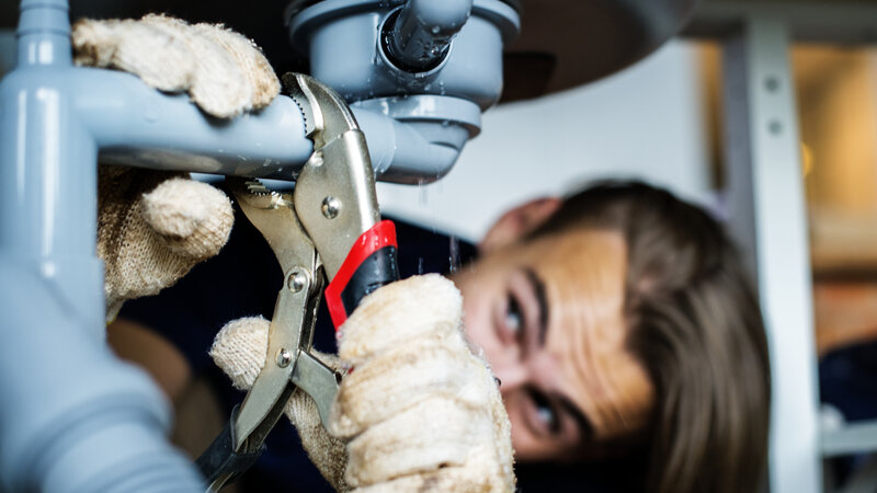 Licensed plumber repairing pipes under kitchen sink in Central Texas home - Warren Brothers Plumbing serves Bastrop, Austin, and Elgin