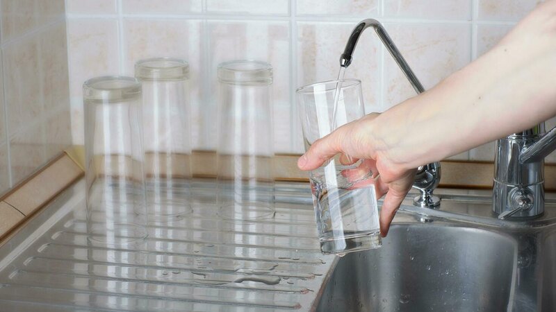 Woman filling glass with clean filtered water from kitchen faucet - Warren Brothers Plumbing serves Bastrop, Austin, and Elgin TX